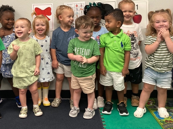 Preschool students standing in a classroom smiling and happy